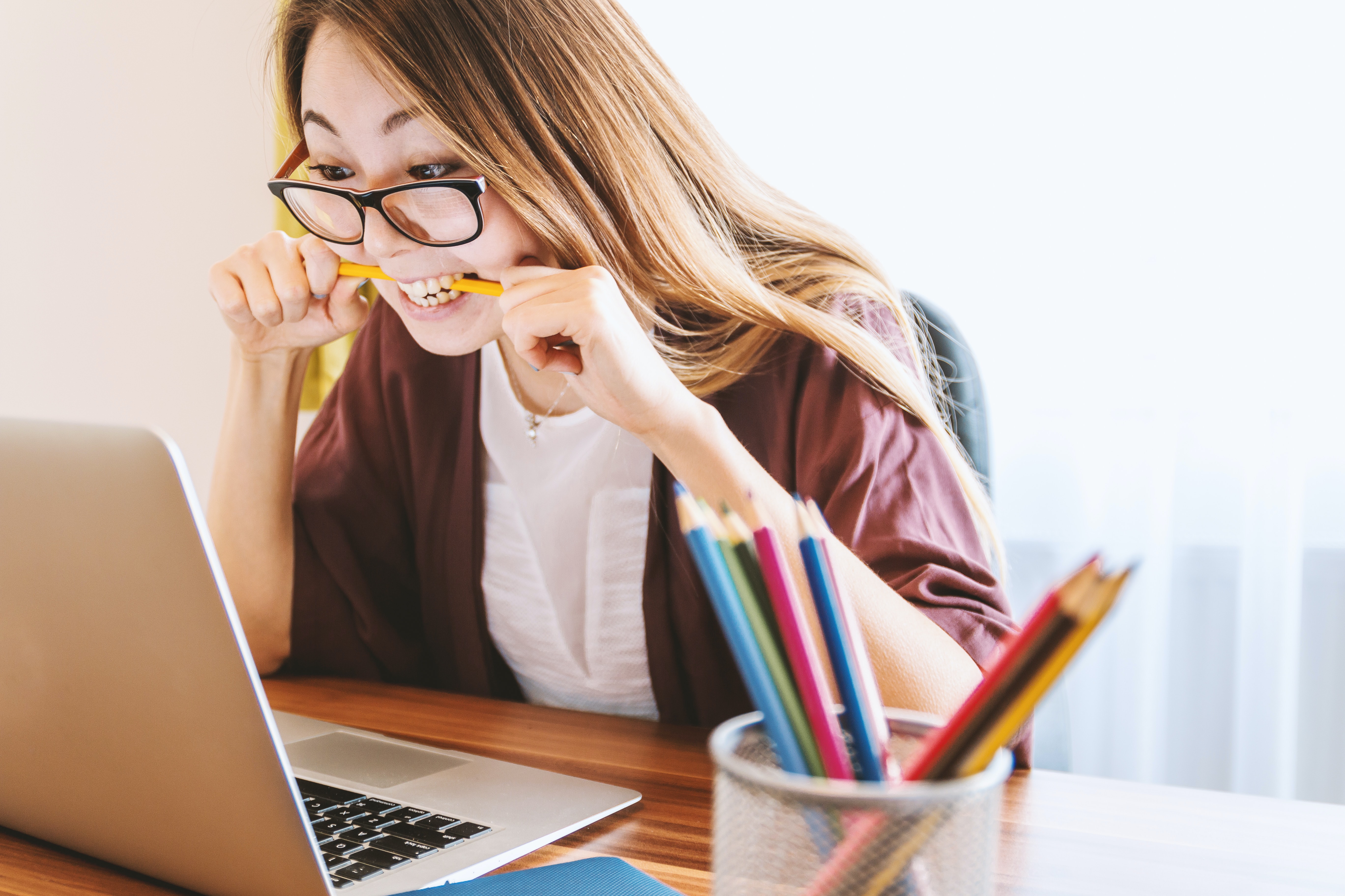 Pictured: woman biting a pen and looking at a laptop screen.