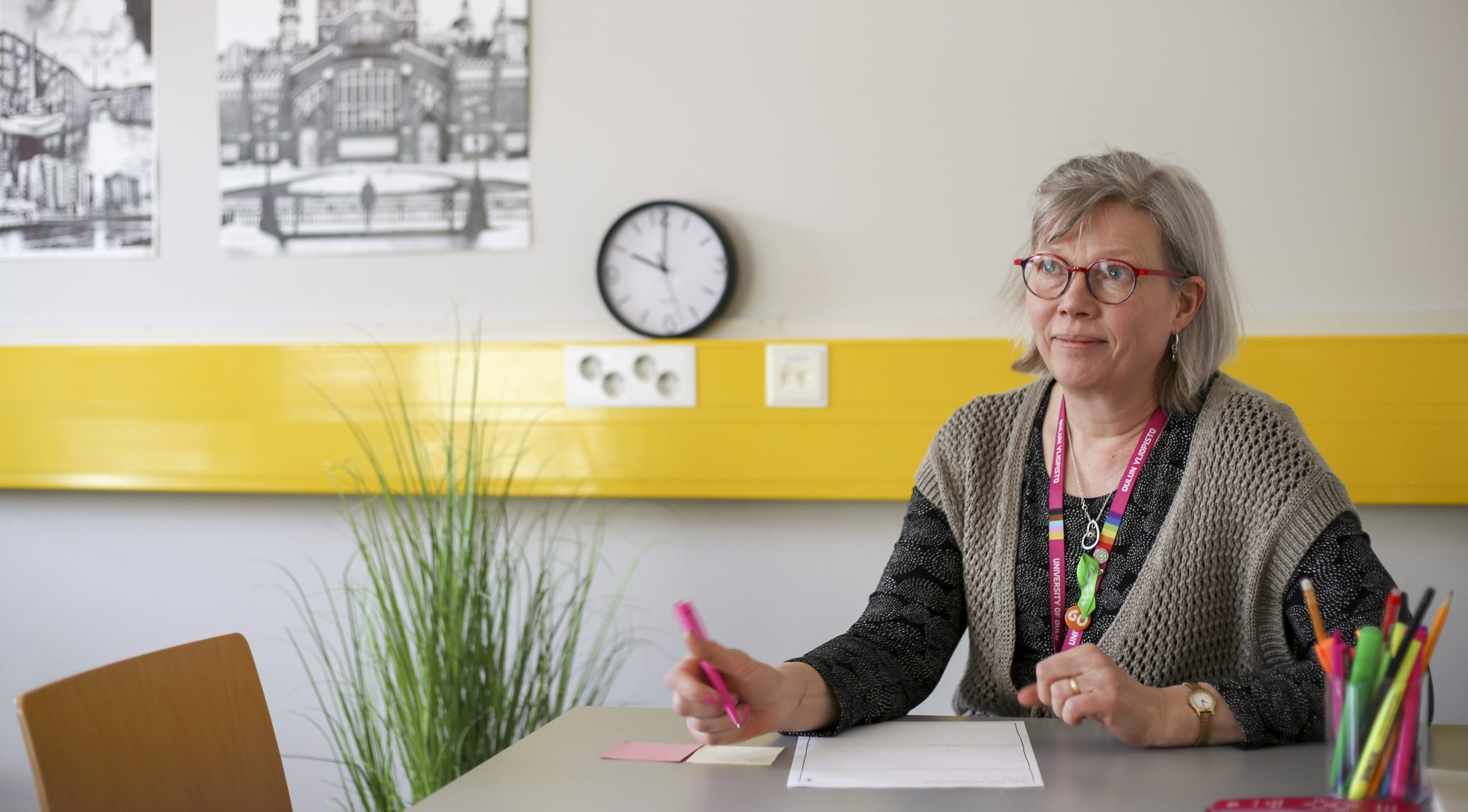 Nainen istuu pöydän ääressä kynä kädessään.